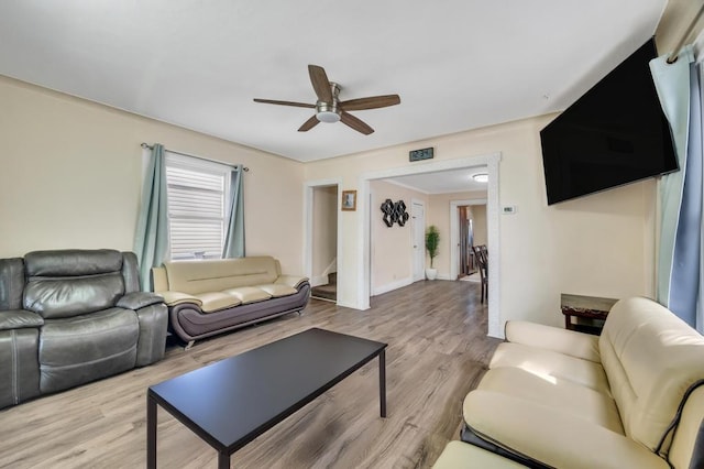 living area with light wood-style flooring, stairs, and a ceiling fan