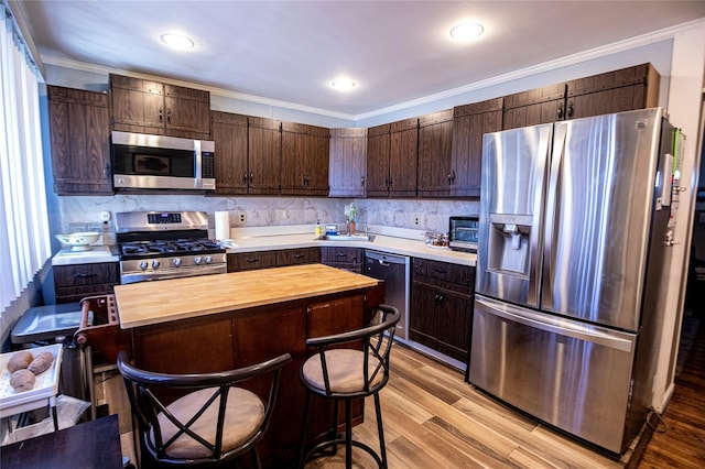 kitchen featuring light wood-type flooring, backsplash, dark brown cabinetry, stainless steel appliances, and butcher block countertops