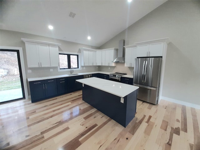 kitchen featuring wall chimney exhaust hood, stainless steel appliances, sink, white cabinets, and a kitchen island