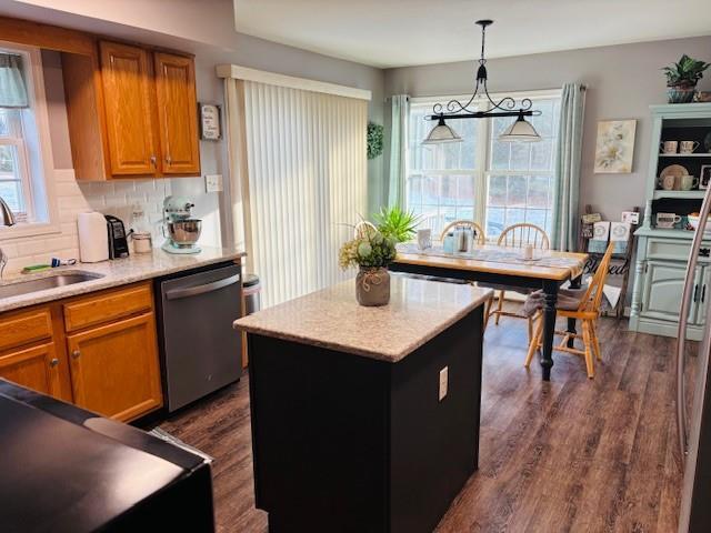 kitchen featuring dark wood-type flooring, sink, pendant lighting, dishwasher, and a center island