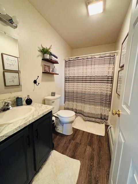 bathroom featuring vanity, hardwood / wood-style flooring, toilet, baseboard heating, and walk in shower