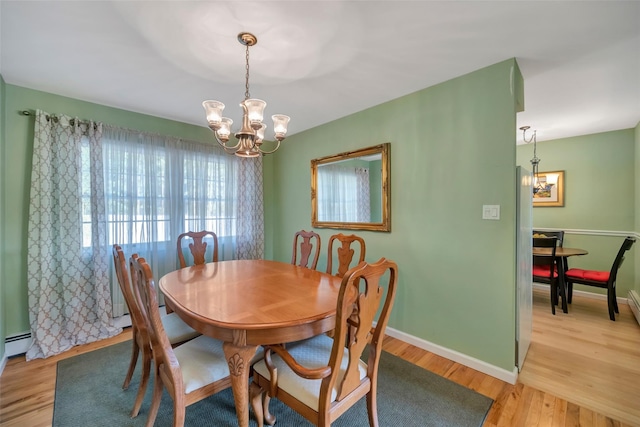 dining room featuring light wood-type flooring, a baseboard heating unit, and a notable chandelier