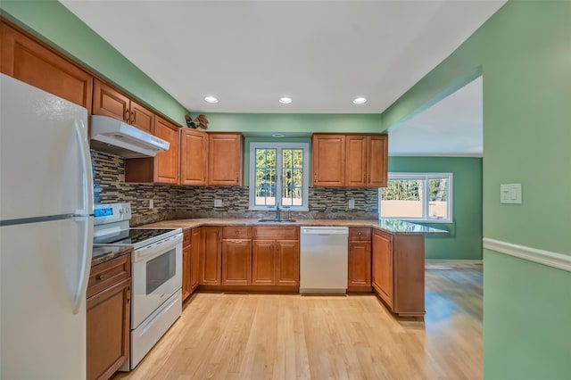 kitchen featuring white appliances, sink, light stone countertops, light wood-type flooring, and kitchen peninsula