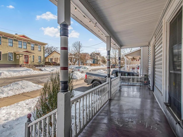 snow covered back of property featuring a residential view and covered porch