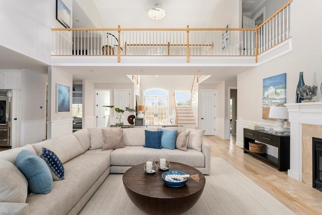 living room featuring a tiled fireplace, light wood-type flooring, and a high ceiling