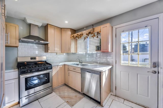 kitchen with light brown cabinetry, light countertops, appliances with stainless steel finishes, wall chimney exhaust hood, and a sink