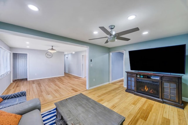 living area with a glass covered fireplace, recessed lighting, wood finished floors, and baseboards