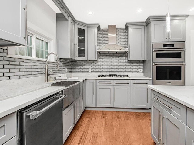 kitchen with gray cabinetry, stainless steel appliances, tasteful backsplash, and wall chimney exhaust hood