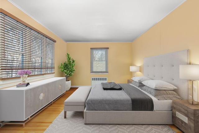 bedroom with light hardwood / wood-style floors, multiple windows, radiator heating unit, and crown molding