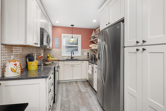 kitchen featuring light hardwood / wood-style floors, sink, white cabinetry, hanging light fixtures, and appliances with stainless steel finishes