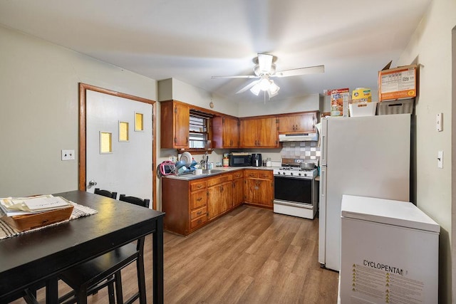 kitchen with white appliances, light wood-type flooring, ceiling fan, decorative backsplash, and sink