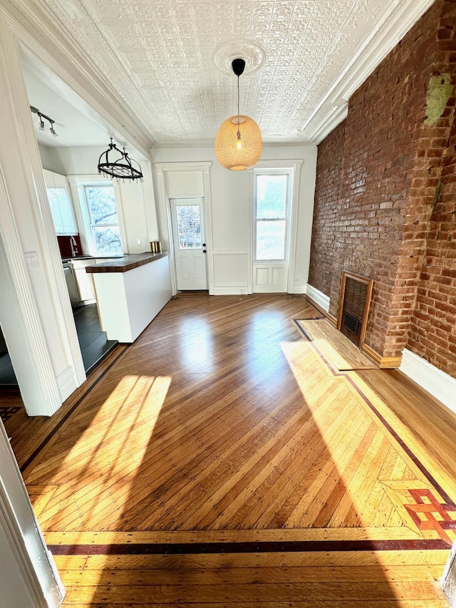 unfurnished living room featuring brick wall, hardwood / wood-style flooring, and crown molding