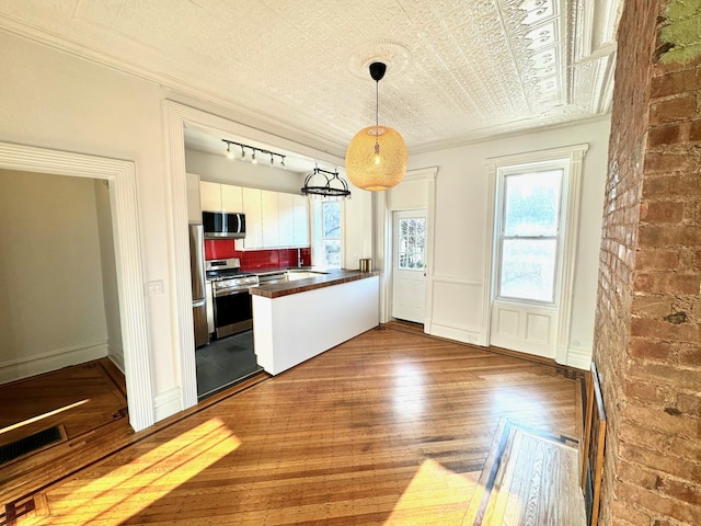 kitchen featuring pendant lighting, hardwood / wood-style floors, crown molding, white cabinets, and appliances with stainless steel finishes