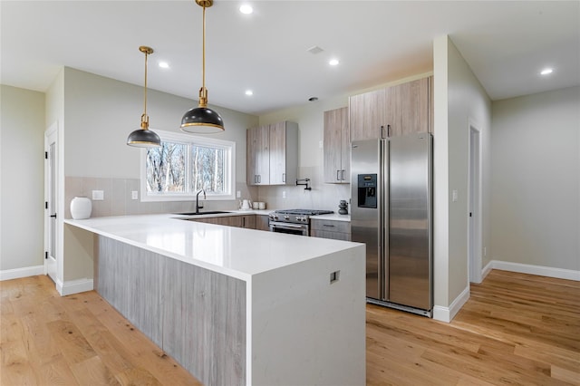 kitchen with sink, light wood-type flooring, kitchen peninsula, pendant lighting, and appliances with stainless steel finishes