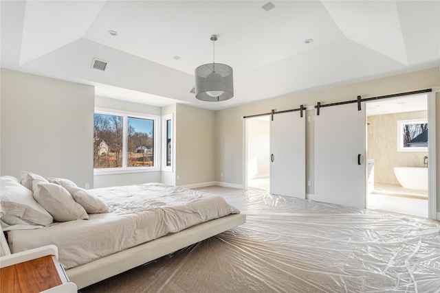 bedroom featuring a raised ceiling, ensuite bath, and a barn door