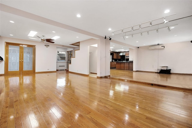 unfurnished living room with ceiling fan, a wall mounted AC, light hardwood / wood-style floors, french doors, and radiator heating unit