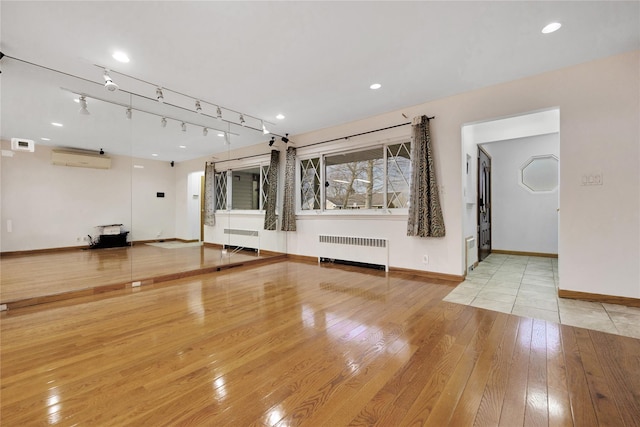 interior space with light hardwood / wood-style flooring, an AC wall unit, and radiator heating unit