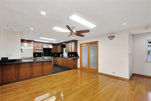 kitchen featuring wall chimney range hood, stainless steel appliances, french doors, kitchen peninsula, and hardwood / wood-style flooring