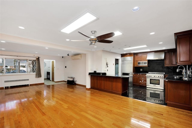 kitchen with hardwood / wood-style flooring, backsplash, built in appliances, radiator, and sink