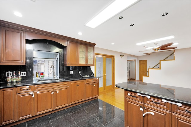 kitchen featuring ceiling fan, sink, backsplash, and dark stone countertops