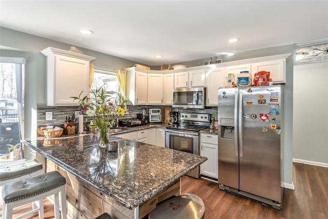 kitchen with white cabinets, appliances with stainless steel finishes, dark stone countertops, and tasteful backsplash