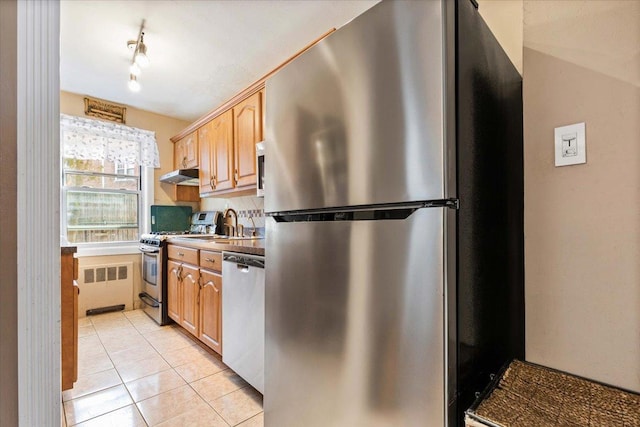 kitchen featuring light tile patterned floors, tasteful backsplash, radiator, light brown cabinetry, and appliances with stainless steel finishes