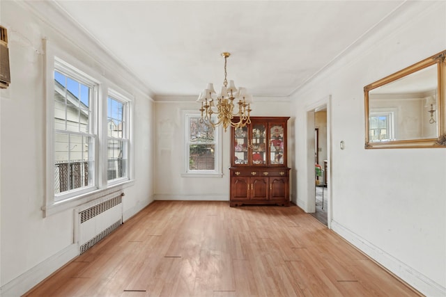 unfurnished dining area featuring ornamental molding, radiator, a chandelier, and light wood-type flooring