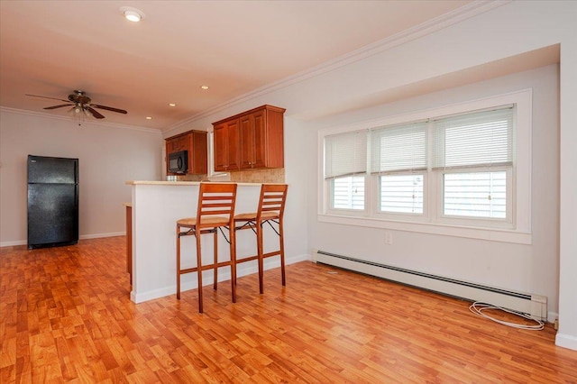 kitchen with a baseboard heating unit, light hardwood / wood-style floors, black appliances, a breakfast bar, and ornamental molding