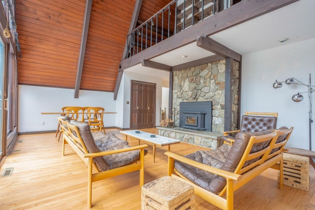 living room with beam ceiling, wooden ceiling, a wood stove, and light hardwood / wood-style flooring