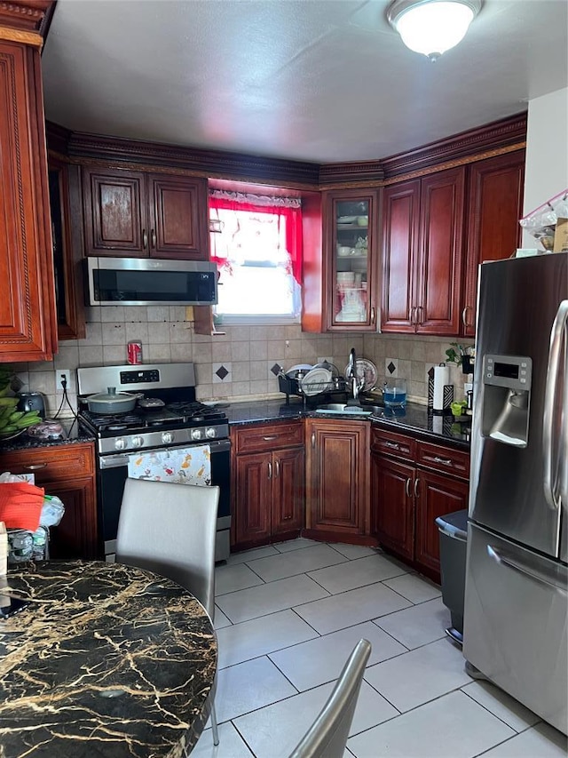 kitchen with light tile patterned floors, sink, dark stone countertops, backsplash, and stainless steel appliances