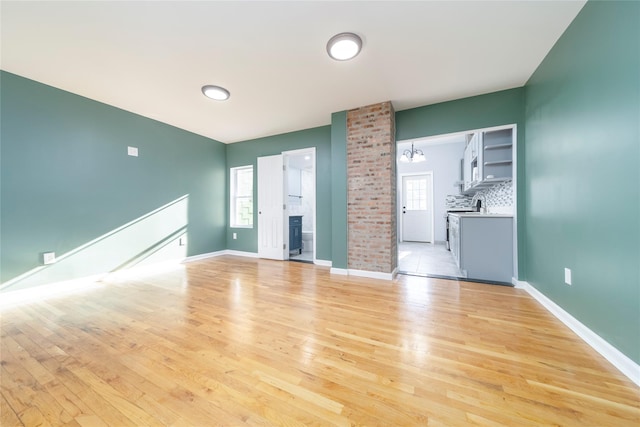 empty room featuring light hardwood / wood-style floors, a brick fireplace, and a chandelier