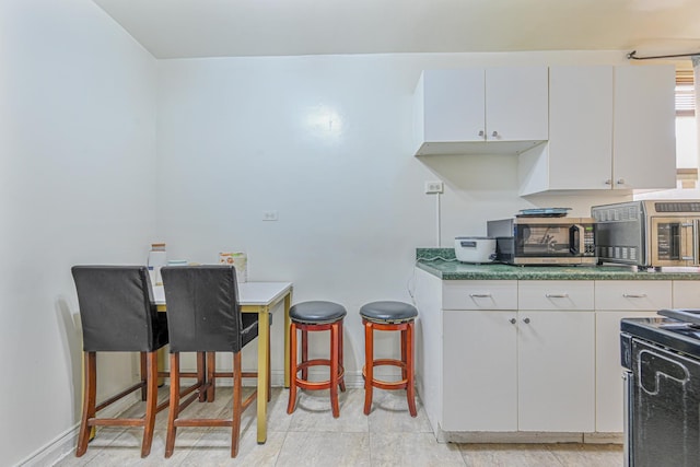 kitchen with white cabinets, a kitchen bar, and black stove