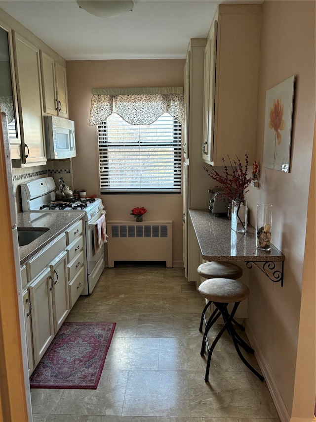 kitchen featuring white appliances, cream cabinetry, and radiator