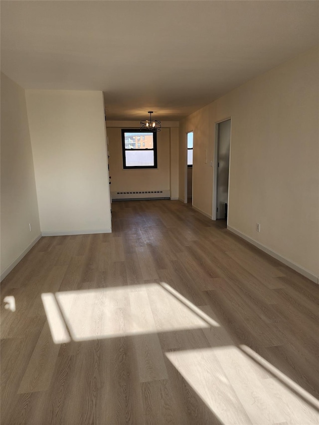 unfurnished room with a baseboard heating unit, hardwood / wood-style flooring, and a chandelier