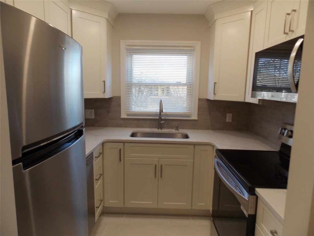 kitchen with stainless steel appliances, white cabinetry, sink, and backsplash