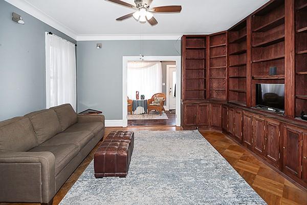 living room featuring dark parquet flooring, ceiling fan, and crown molding