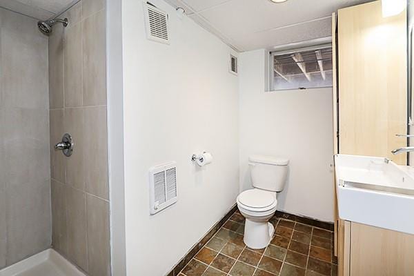 bathroom with toilet, a tile shower, and vanity