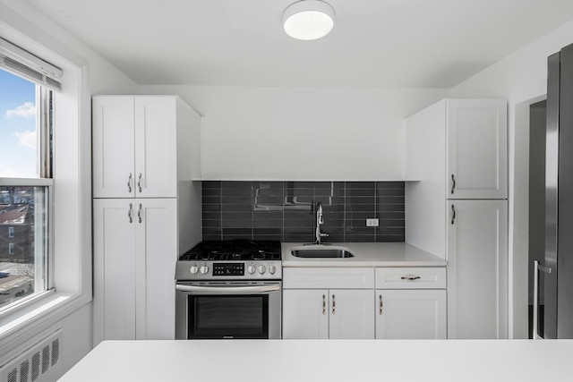 kitchen featuring sink, white cabinets, radiator heating unit, backsplash, and gas stove