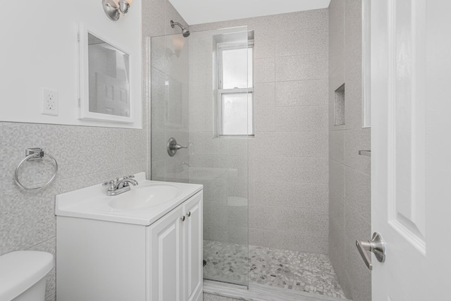 bathroom featuring tile walls, a tile shower, vanity, and toilet