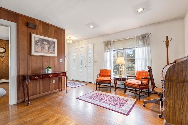 living area with wooden walls, baseboard heating, and light hardwood / wood-style flooring