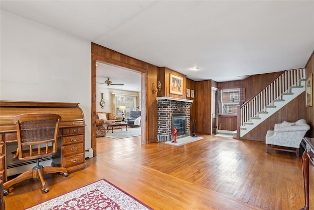 interior space featuring a brick fireplace, baseboard heating, ceiling fan, and hardwood / wood-style flooring