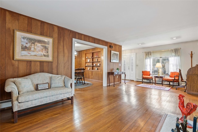 living room with built in shelves, a baseboard radiator, and hardwood / wood-style floors