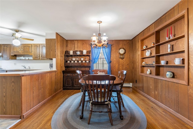 dining space with light hardwood / wood-style floors, wooden walls, built in features, and ceiling fan with notable chandelier