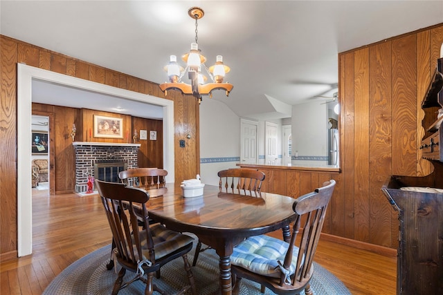 dining space with ceiling fan with notable chandelier, wood walls, a fireplace, and wood-type flooring