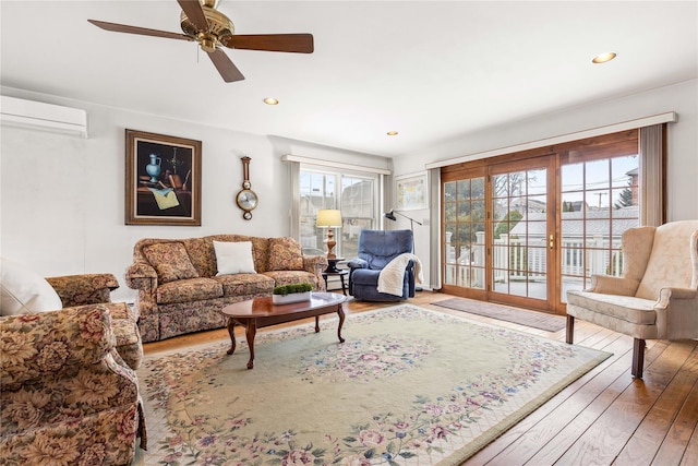 living room featuring wood-type flooring, ceiling fan, and an AC wall unit