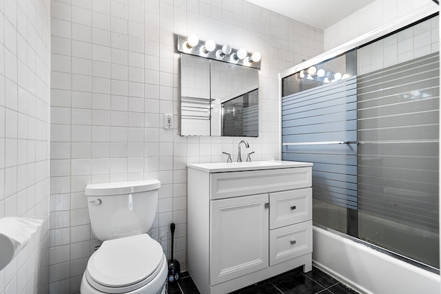 full bathroom featuring toilet, tile patterned floors, combined bath / shower with glass door, and tile walls