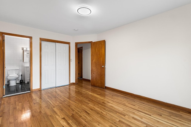 unfurnished bedroom featuring light hardwood / wood-style flooring, ensuite bathroom, and a closet