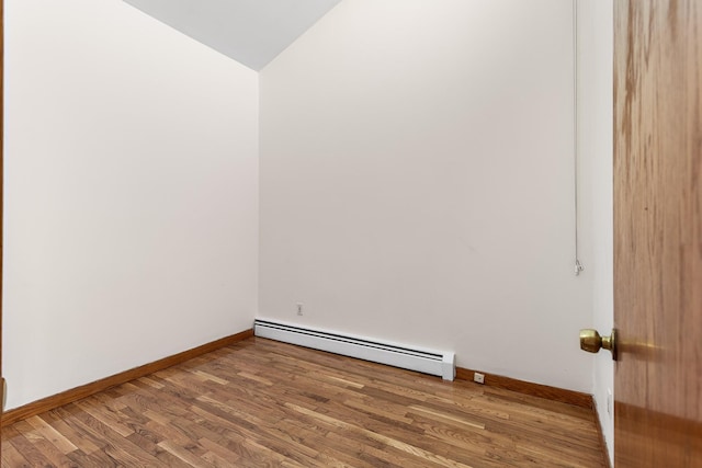 empty room with wood-type flooring, baseboard heating, and vaulted ceiling