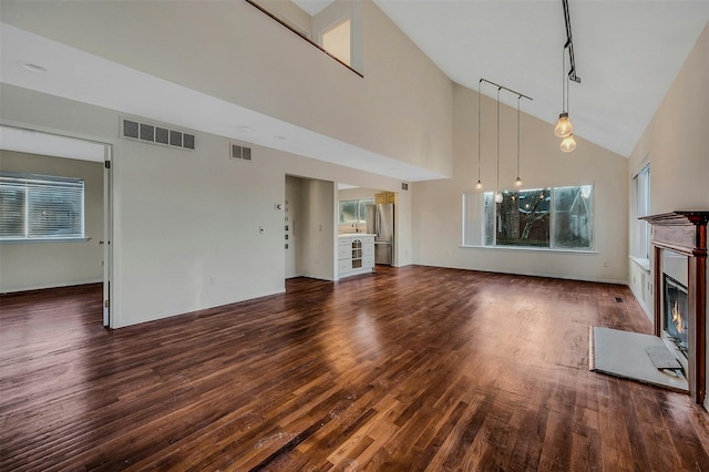 unfurnished living room with track lighting, high vaulted ceiling, and dark hardwood / wood-style flooring