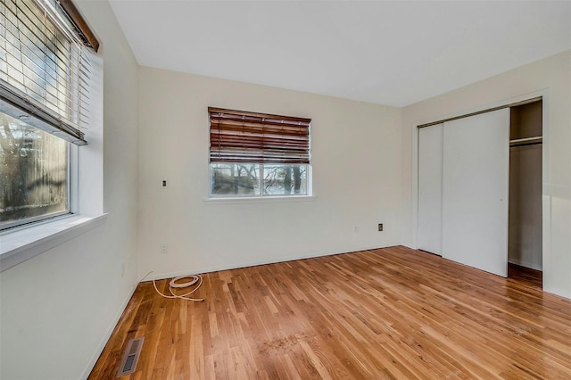 unfurnished bedroom featuring light wood-type flooring, a closet, and multiple windows